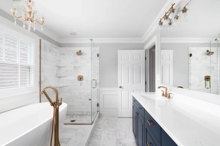 Bright bathroom with freestanding bathtub, glass shower with marble tiles and navy vanity