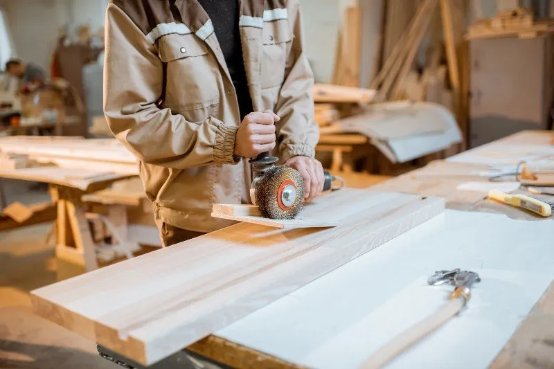 Carpenter sanding a wooden plank in workshop
