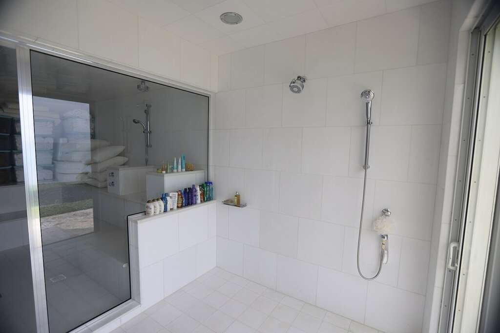 Bright walk in shower with clean white tiles, a handheld shower head and a glass screen