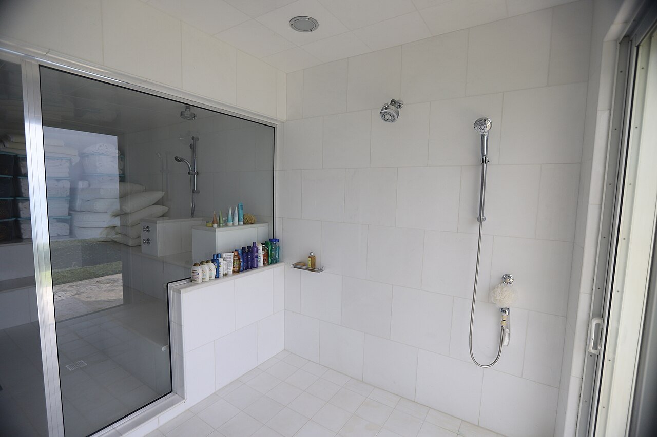 Bright walk in shower with clean white tiles, a handheld shower head and a glass screen
