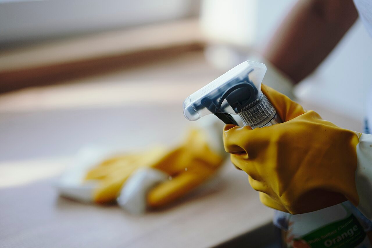 A gloved hand spraying cleaner from a spray bottle while cleaning tiles.