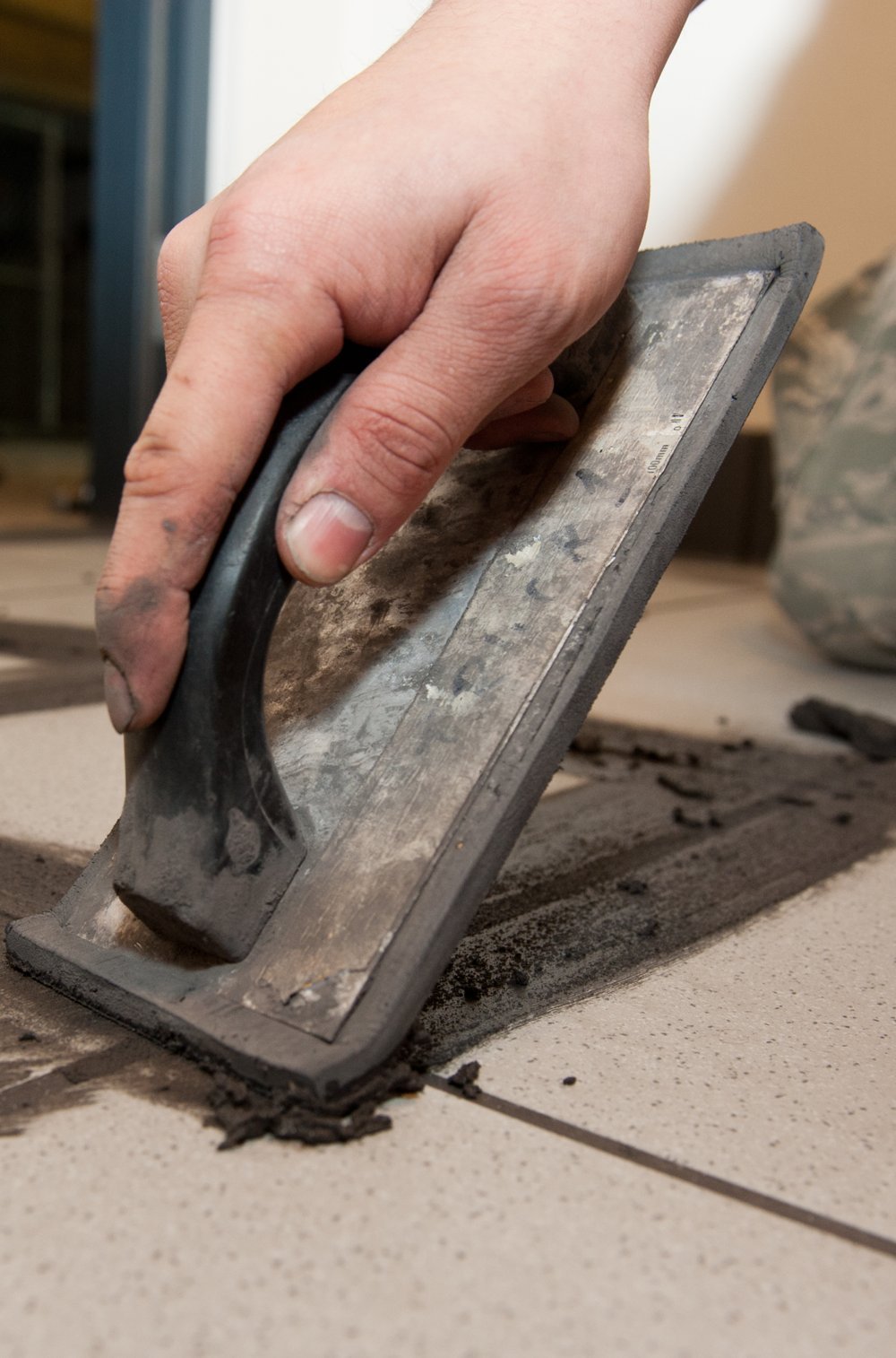 Worker applying grout to new floor tiles during a tile installation in St. Catharines, Ontario, by BGM Construction LTD