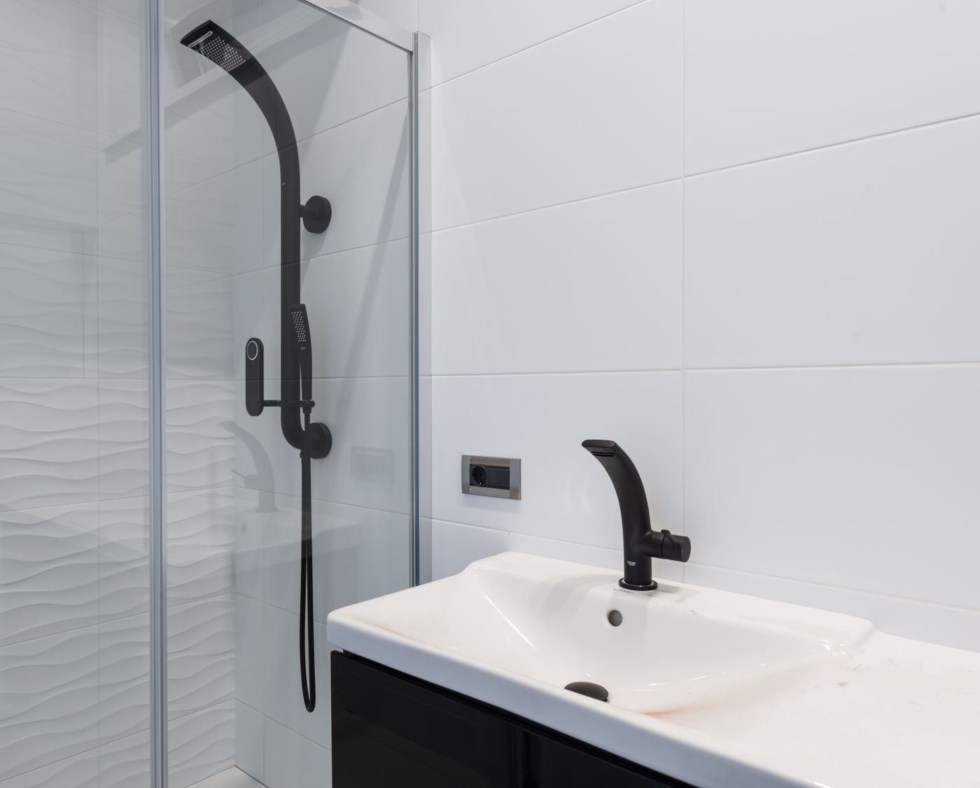Large white wall tiles with light gray grout lines and black fixtures in a modern bathroom.